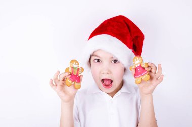 Noel Baba şapkalı bir çocuk beyaz arka planda Noel kurabiyesi tutuyor. Noel ve yeni yıl konsepti