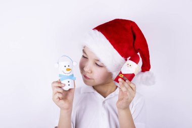 Noel Baba şapkalı bir çocuk beyaz arka planda Noel zanaatı tutuyor. Noel ve yeni yıl konsepti