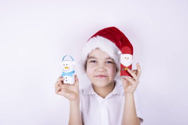 Noel Baba şapkalı bir çocuk beyaz arka planda Noel zanaatı tutuyor. Noel ve yeni yıl konsepti