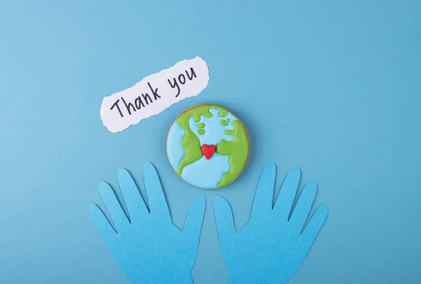 Thank you sign with paper hands in blue gloves on a medical background. gingerbread planet earth with a red heart