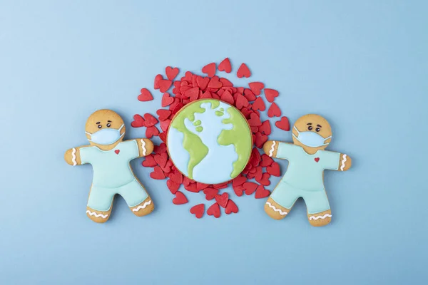 gingerbread doctors in a medical mask, planet earth with red hearts on a blue background. the concept of wearing masks and the coronavirus pandemic