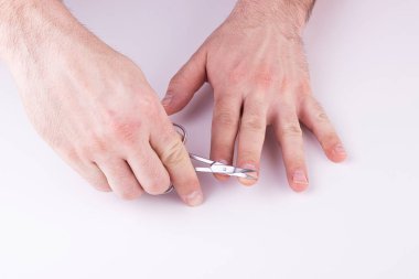 Erkeklerin elleri beyaz arka planda tırnaklarını makasla kesiyor. Erkek manikürü, el bakımı.