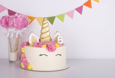 Beyaz arka planda pembe lolipopları olan beyaz, narin tek boynuzlu at pastası. Doğum günü pastası