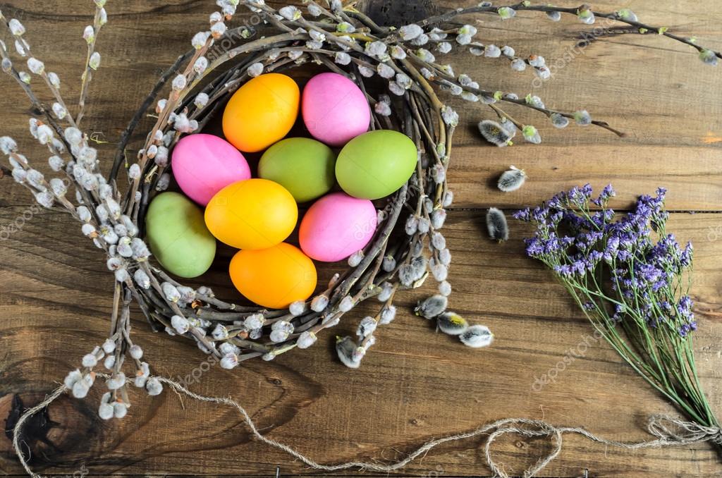 Easter eggs in willow nest, flowers over wooden rustic background