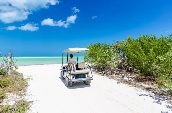 Joven conduciendo en un carrito de golf en la playa tropical de arena blanca — Foto de Stock