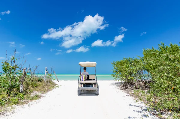 Ung man kör på en golfbil på tropical vit sandstrand — Stockfoto