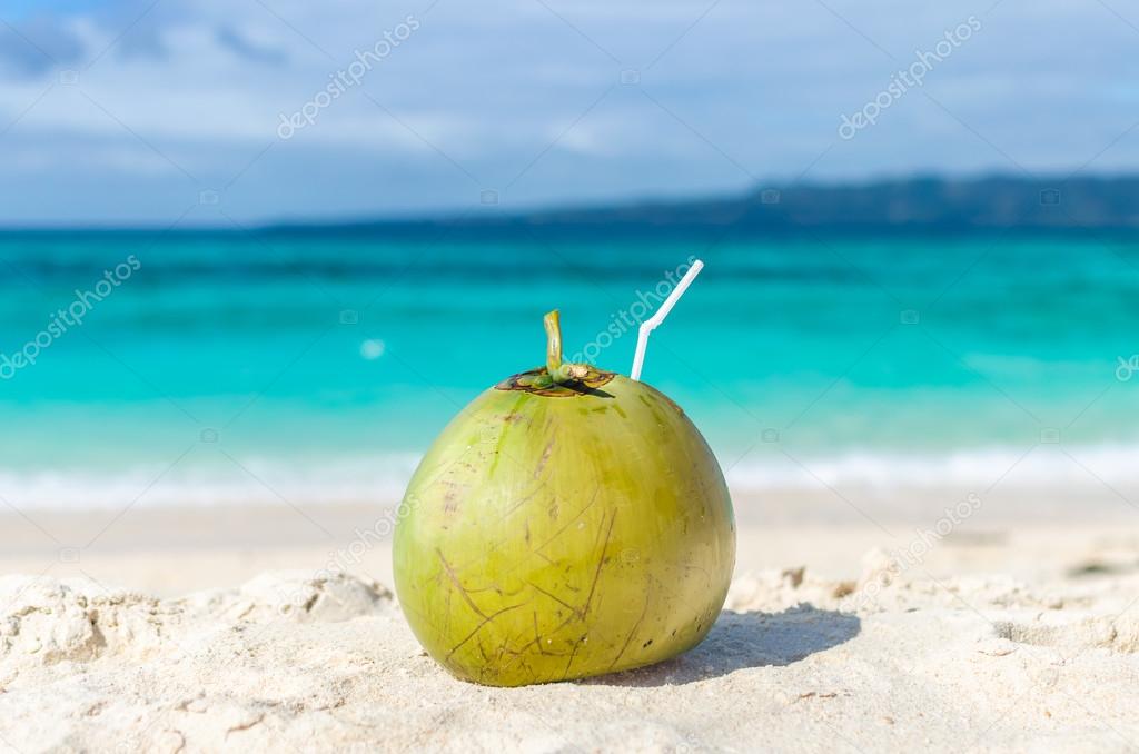 Tropical green coconut with straw on white exotic sandy beach 