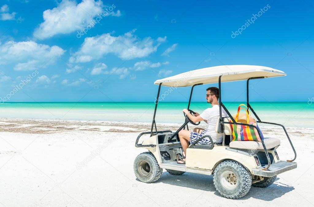 Young man driving golf cart along tropical sandy beach during his Caribbean vacation