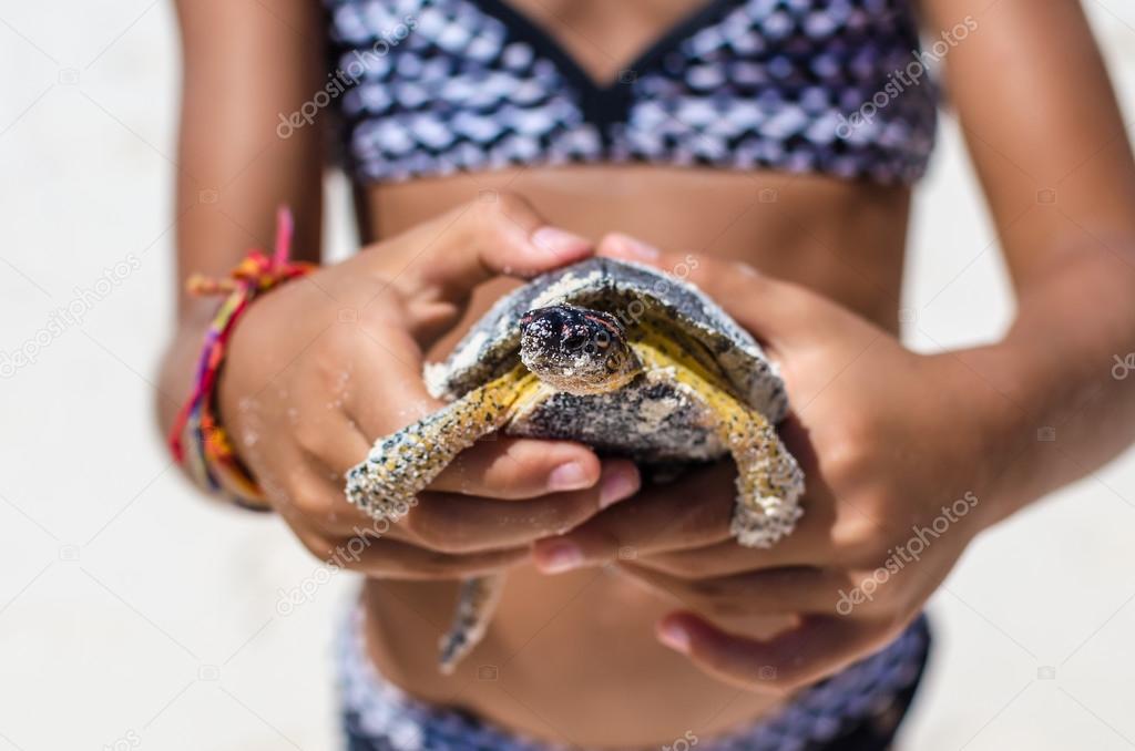 Young girl playing with turtle in hand against the background of tropical white sandy beach