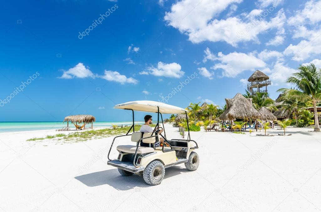 Young man driving golf cart along tropical white sandy beach during his Caribbean vacation on Holbox