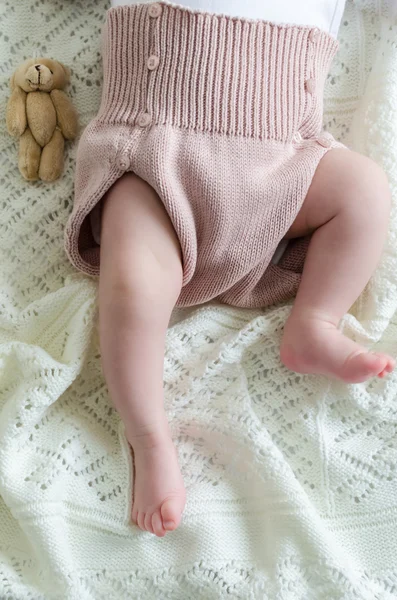 Kleine kleine baby's voeten in wollen korte broek met een stuk speelgoed — Stockfoto