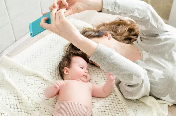 Mãe e filhinha tomando uma selfie na cama em casa — Fotografia de Stock