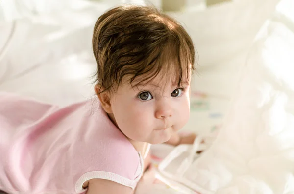 Süßes kleines Mädchen, das in die Kamera schaut und auf dem Bett liegt — Stockfoto