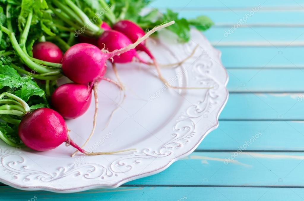 A bunch of fresh radish on plate over rustic wooden turquoise table background