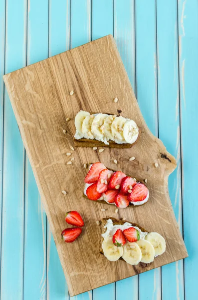 Bruschetta con queso ricotta, fresa y plátano sobre mesa de madera turquesa — Foto de Stock