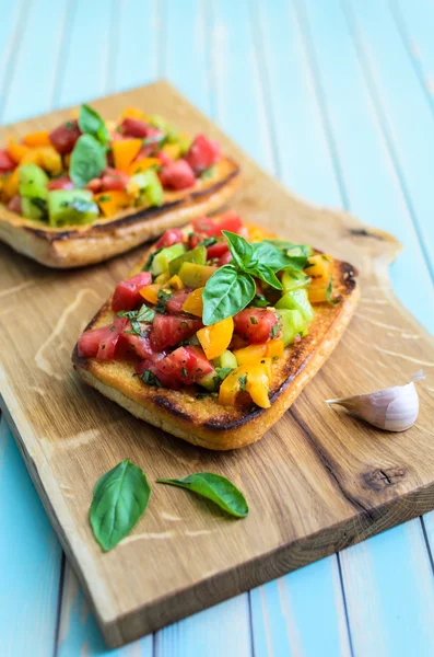 Bruschetta italiana con tomates picados y albahaca sobre tabla de cortar de madera —  Fotos de Stock