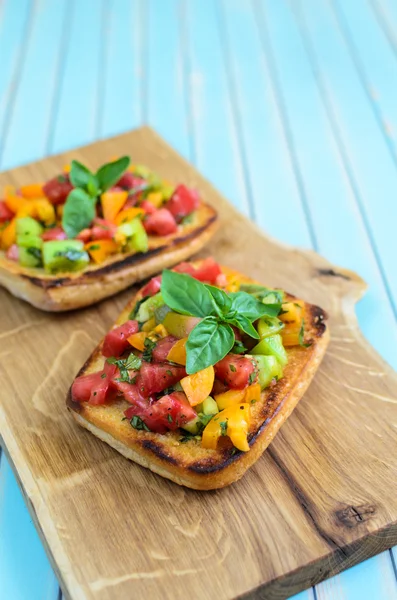 Bruschetta italiana con tomates picados y albahaca sobre tabla de cortar de madera —  Fotos de Stock