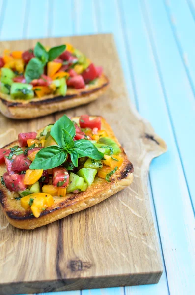 Bruschetta italiana con tomates picados y albahaca sobre tabla de cortar de madera —  Fotos de Stock