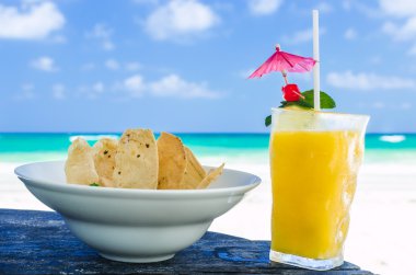 Fresh cocktail with orange juice and nachos on table at tropical exotic Caribbean beach