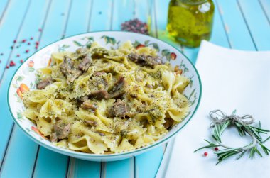 Pasta farfalle with turkey, pesto sauce and rosemary in serving plate over wooden turquoise background