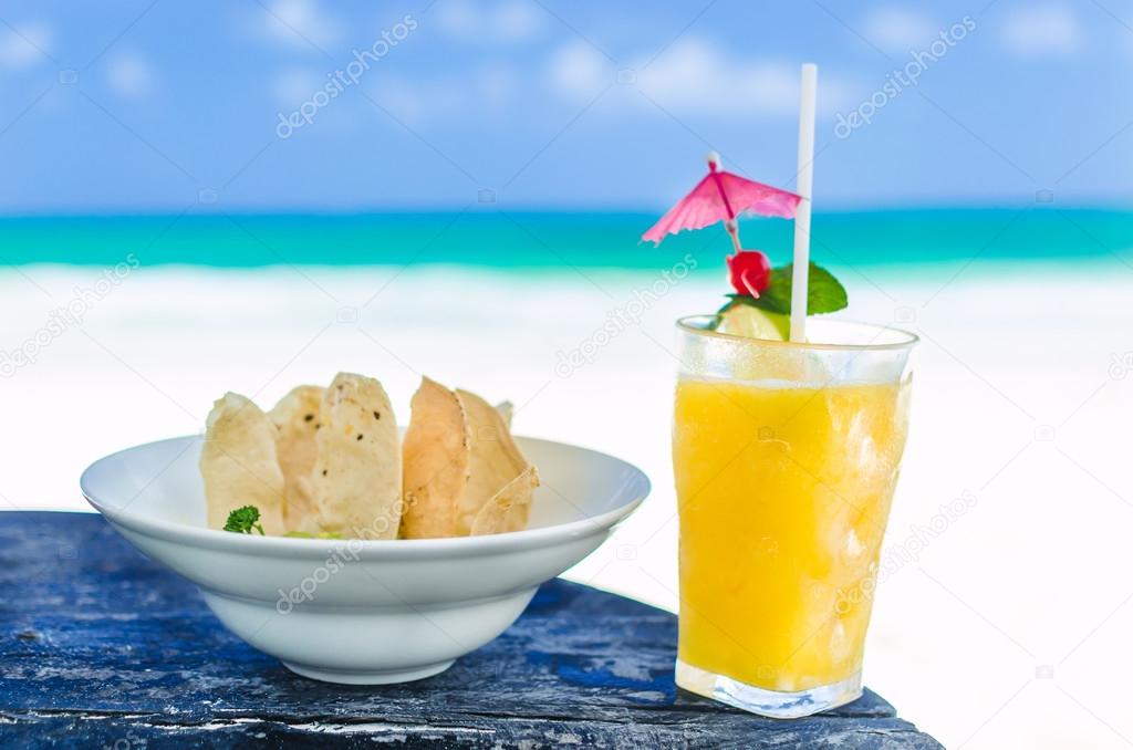 Fresh cocktail with orange juice and nachos on table at tropical exotic Caribbean beach