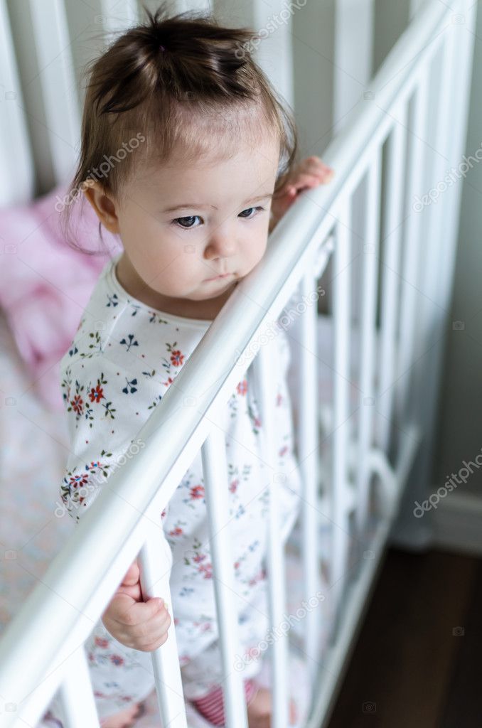 Portrait of adorable little baby girl staying at her bed in full-length