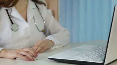 Kadın doktor laptopta sayfaları karıştırıyor, mektup yazıyor, hastalara danışmanlık yapıyor.