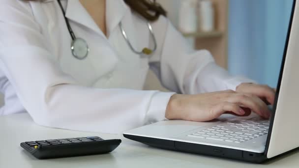 Жінка-лікар заповнює форму медичного страхування на ноутбуці, обчислюючи витрати — стокове відео
