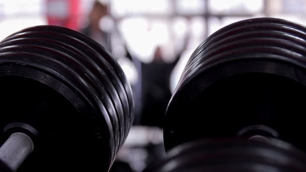 Primo piano di manubri in palestra, uomo attivo fuori fuoco che fa esercizi — Video Stock