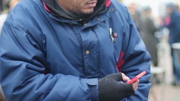 Hombre vistiendo ropa de mala calidad mirando cautelosamente a su alrededor en multitud, usando un teléfono inteligente — Vídeos de Stock