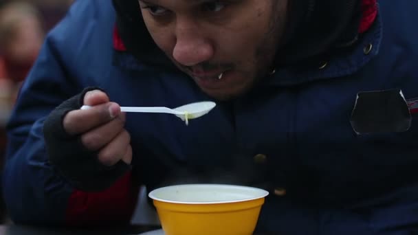 Hambriento indigente comiendo alimentos donados por voluntarios, evento de caridad para los pobres — Vídeos de Stock