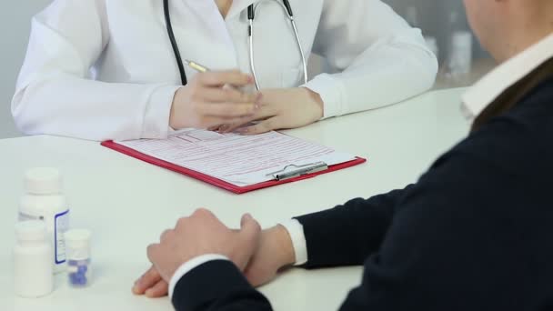Doctora cuestionando paciente masculino, poniendo datos en documentos de seguro — Vídeos de Stock