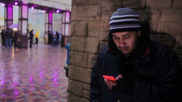 Un hombre enfermo esperando a alguien en la calle. Clima frío. Jugando por teléfono — Vídeos de Stock