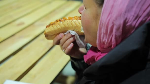 Бедная и голодная женщина ест жирный хот-дог. Нездоровая еда. Проблемы со здоровьем, ожирение — стоковое видео