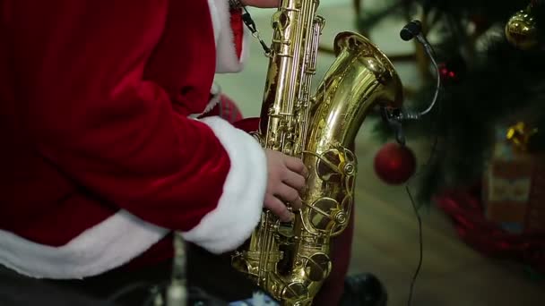 Hombre con traje de Santa Claus tocando villancico en saxofón en concierto festivo — Vídeo de stock
