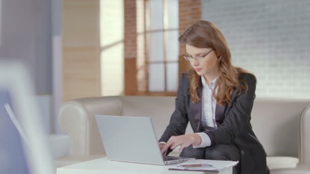 La señora en el traje de trabajo, las gafas trabaja en el portátil, sonríe a la cámara — Vídeo de stock