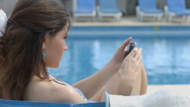 Pretty brunette female browsing internet on smartphone near pool — Stock Video