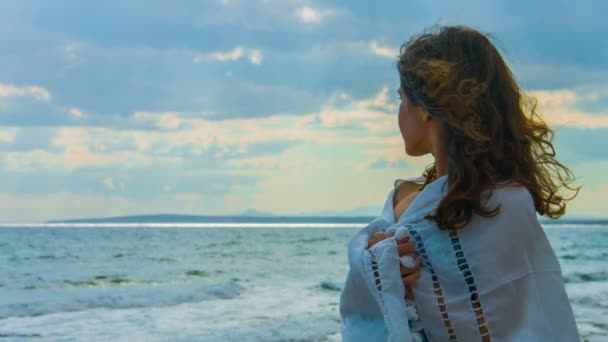 Eenzame mooie vrouw bedekt met sjaal permanent in de buurt van zee, kijkend naar storm — Stockvideo