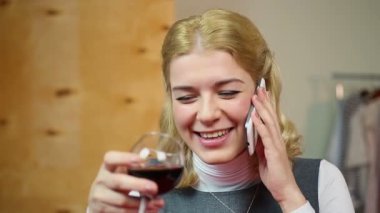 Cep telefonu üzerinde konuşurken, şarap içme ve gülümseyen sarışın kadın gülüyor