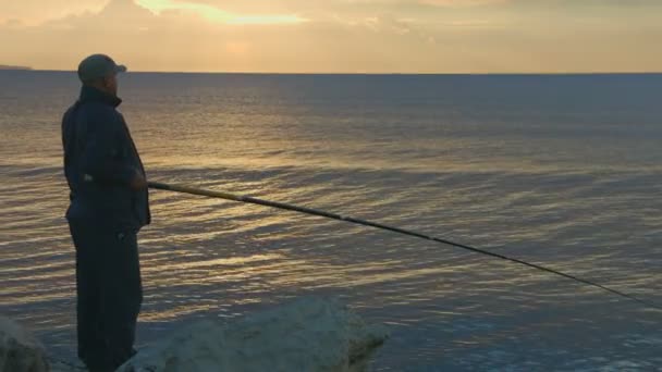 Elderly man fishing with rod from a rocky ocean shore, active rest, magic hour — Stock Video