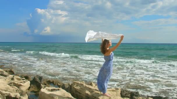 Mujer parada en la orilla del mar, bufanda blanca agitando en el viento. Símbolo de libertad — Vídeo de stock