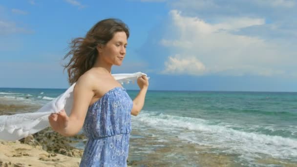 Feliz morena sonriente sosteniendo bufanda blanca en el viento. Día soleado en la orilla del mar — Vídeos de Stock