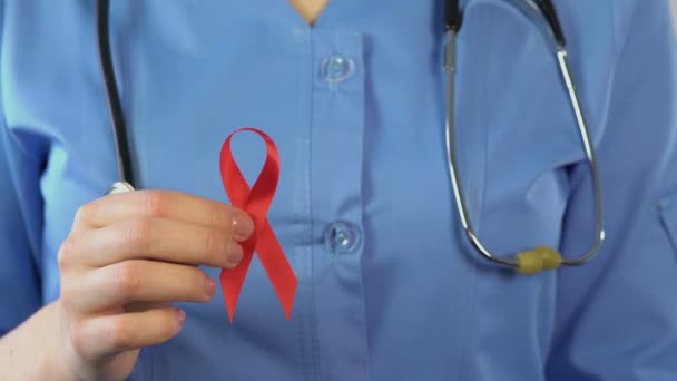 Doktor ukazuje červenou stužku a kondom, mezinárodní symbol povědomí Aids — Stock video