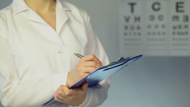 Augenärztin untersucht Patientin, schreibt Diagnose und Behandlung auf — Stockvideo