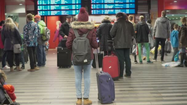 PRAGUE, RÉPUBLIQUE TCHÈQUE - CIRCA DÉCEMBRE 2015 : Passagers à la gare. Jeune femme avec sac à dos debout dans la salle d'attente, en regardant l'horaire des trains — Video