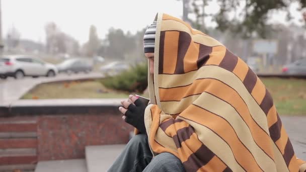 Olyckliga manliga luffare sitter ensam i kylan gatan, uppvärmningen med kaffe och filt — Stockvideo