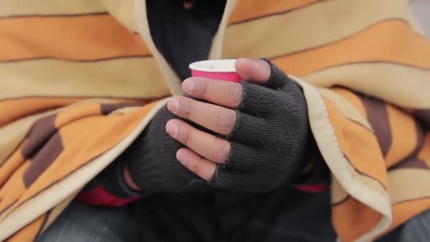 Руки нуждающегося держат теплый напиток в бумажной чашке, крупным планом. Проблема бедности — стоковое видео