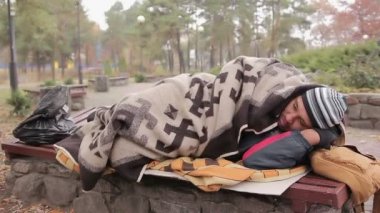 Zavallı evsiz erkek soğuk şehir parkta bankta yalan eski battaniye ile örtülü