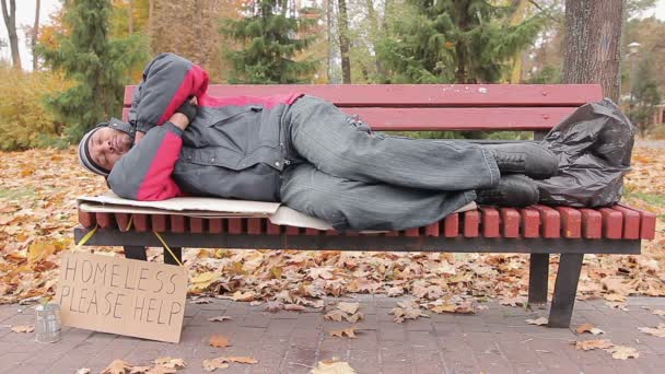 Uomo bisognoso che dorme sulla panchina nel parco autunnale, senzatetto in attesa di aiuto — Video Stock