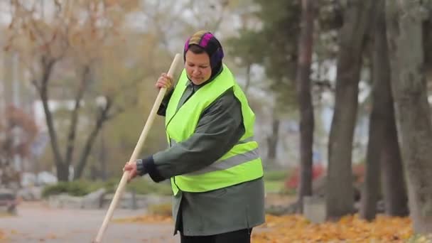 Mujer infeliz con sobrepeso barriendo el parque de la ciudad en otoño, persona trabajadora — Vídeos de Stock